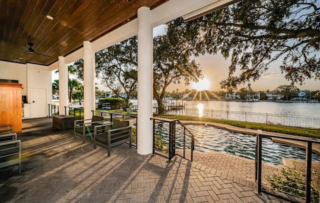 patio terrace at dusk featuring ceiling fan and a water view