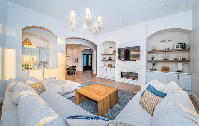 living room with built in shelves, an inviting chandelier, light hardwood / wood-style floors, and a tile fireplace