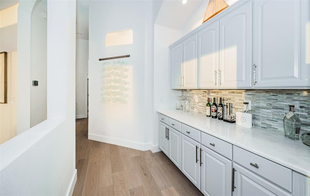 bar with tasteful backsplash, white cabinets, and light wood-type flooring