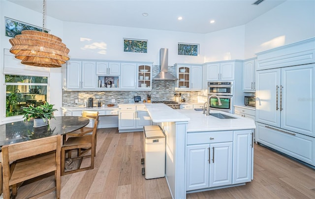 kitchen featuring pendant lighting, sink, a kitchen island with sink, paneled built in fridge, and wall chimney exhaust hood