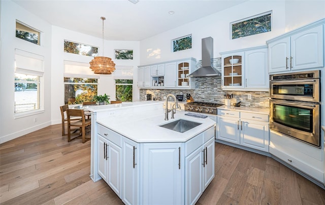 kitchen with wall chimney exhaust hood, sink, pendant lighting, a kitchen island with sink, and backsplash