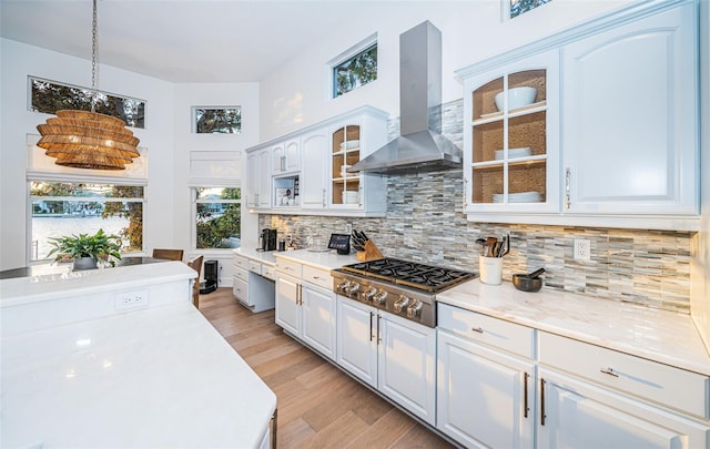 kitchen with wall chimney range hood, hanging light fixtures, tasteful backsplash, white cabinets, and stainless steel gas stovetop