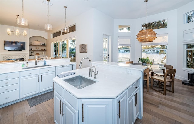 kitchen with a kitchen island with sink, sink, decorative light fixtures, and white cabinets