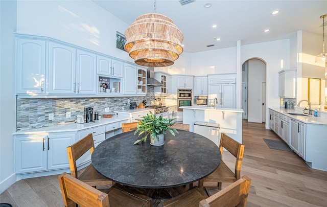 dining area featuring a high ceiling, sink, an inviting chandelier, and light hardwood / wood-style floors