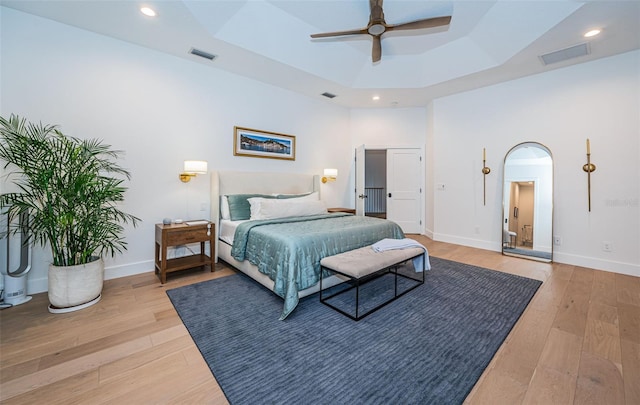 bedroom with ceiling fan, a raised ceiling, hardwood / wood-style floors, and a high ceiling