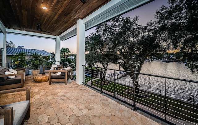 patio terrace at dusk featuring a water view, a balcony, outdoor lounge area, and ceiling fan