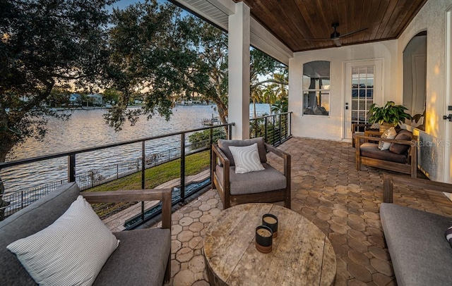 patio terrace at dusk featuring a balcony, a water view, and ceiling fan