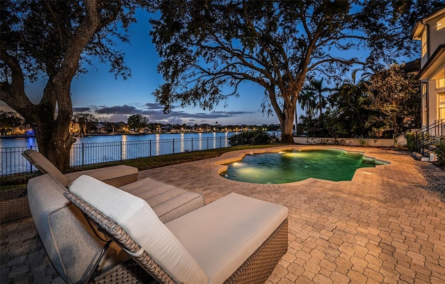 pool at dusk featuring a water view and a patio area