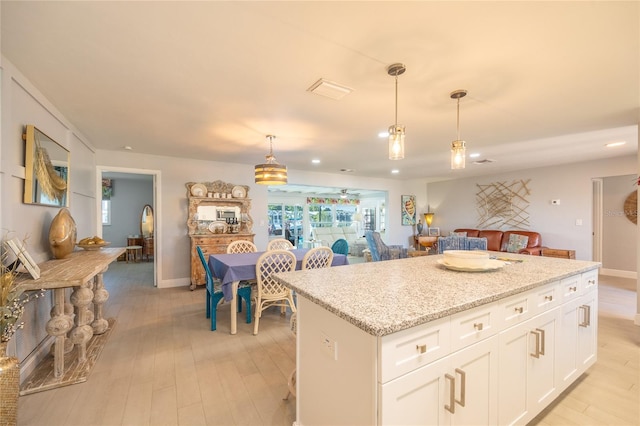 kitchen with pendant lighting, white cabinets, light stone countertops, light hardwood / wood-style floors, and a kitchen island