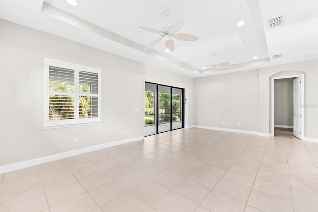 tiled empty room with a healthy amount of sunlight, a raised ceiling, and ceiling fan