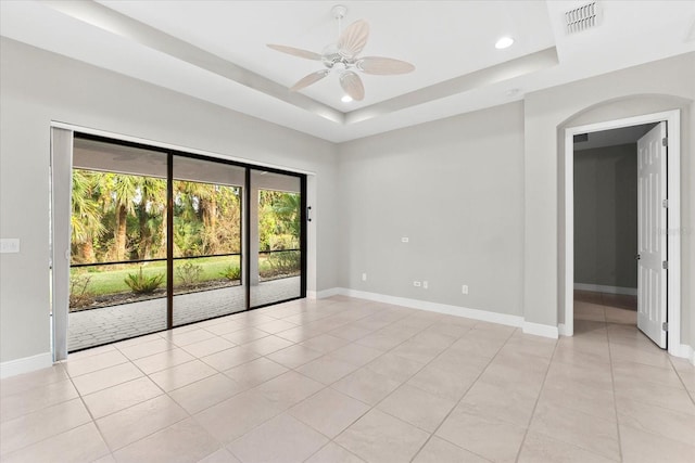 tiled empty room featuring a tray ceiling and ceiling fan