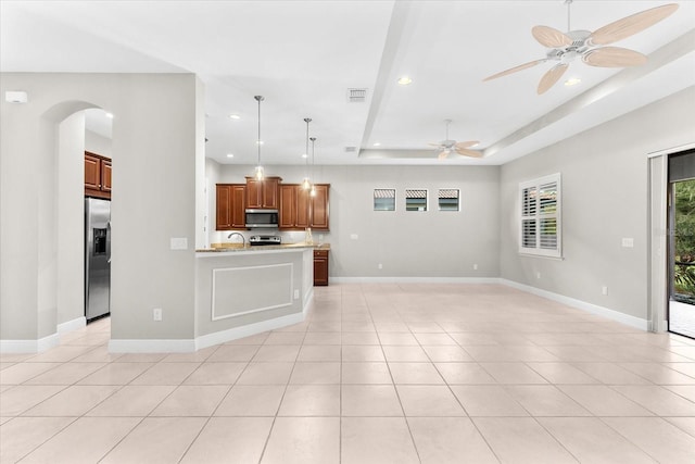 kitchen featuring light stone counters, appliances with stainless steel finishes, decorative light fixtures, light tile patterned floors, and a tray ceiling