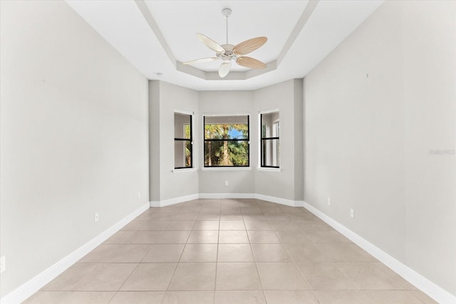 tiled empty room with ceiling fan and a raised ceiling