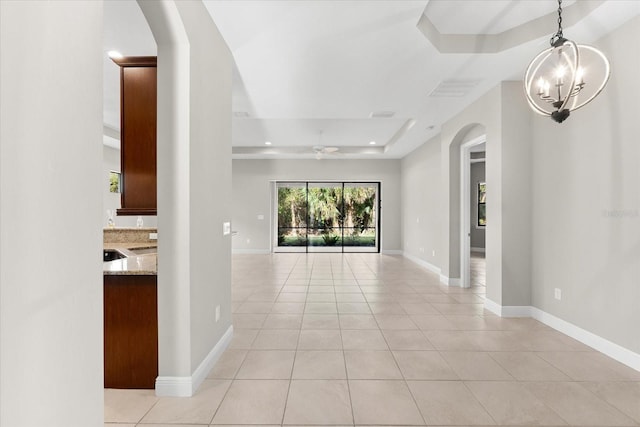 corridor featuring an inviting chandelier, light tile patterned flooring, and a raised ceiling