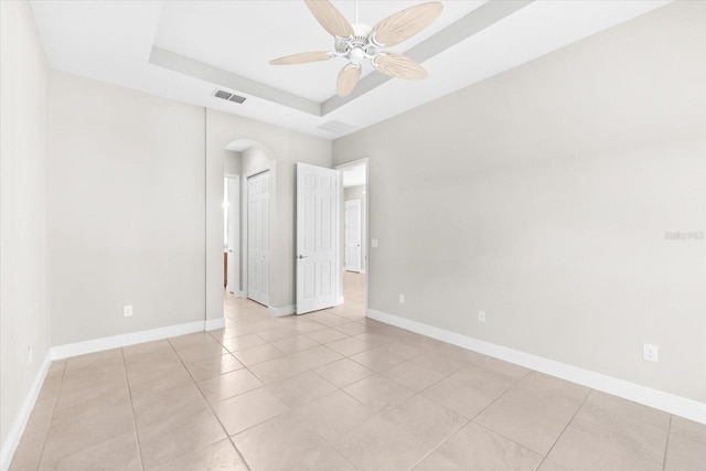 tiled empty room featuring ceiling fan and a raised ceiling