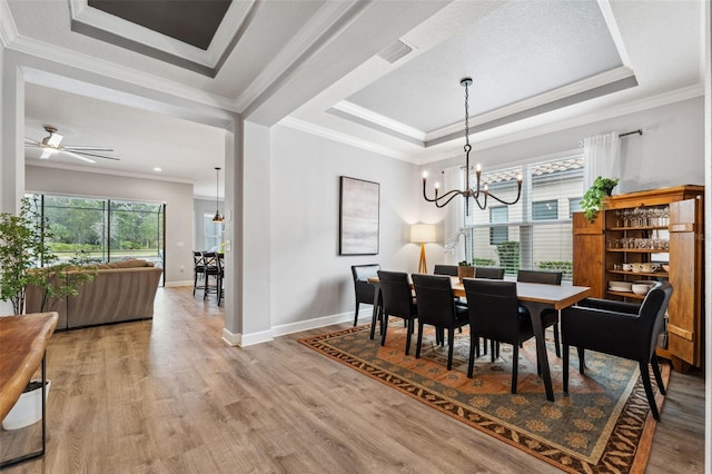 dining area featuring wood-type flooring, ceiling fan with notable chandelier, a raised ceiling, and ornamental molding