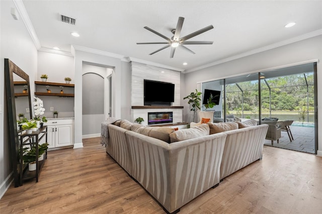 living room featuring ceiling fan, a fireplace, ornamental molding, and light wood-type flooring