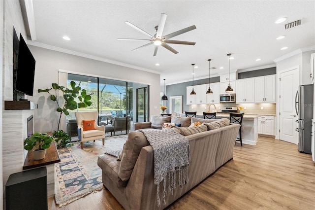 living room featuring ceiling fan, ornamental molding, and light wood-type flooring