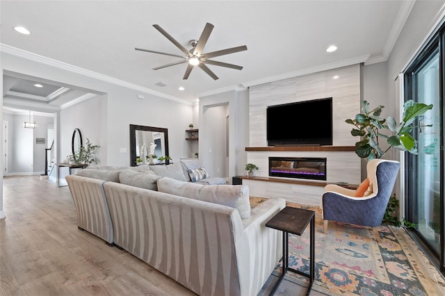 living room with crown molding, a large fireplace, ceiling fan, and light hardwood / wood-style flooring