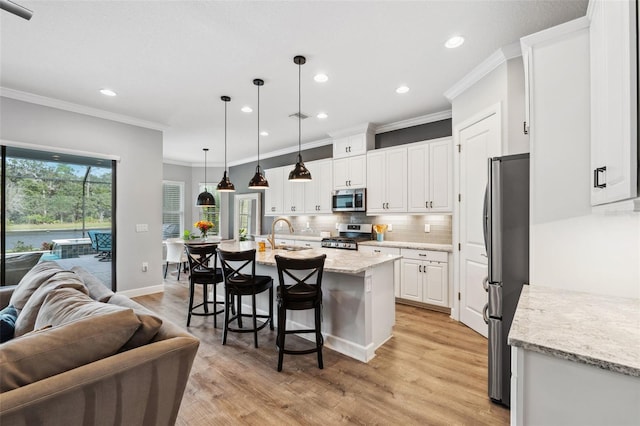 kitchen featuring light hardwood / wood-style flooring, an island with sink, appliances with stainless steel finishes, decorative light fixtures, and white cabinetry