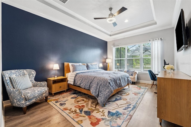 bedroom featuring wood-type flooring, a raised ceiling, ceiling fan, and ornamental molding