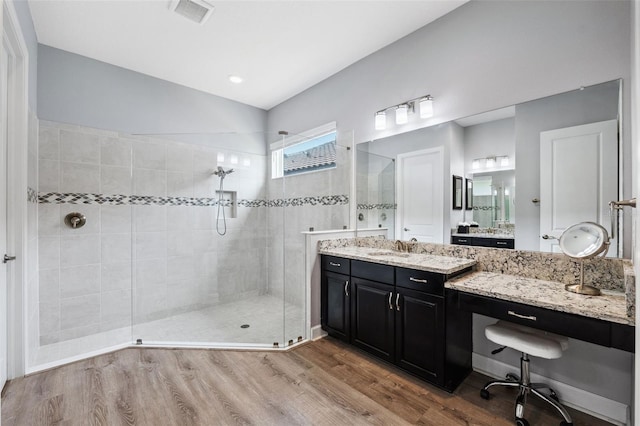 bathroom with a tile shower, vanity, and wood-type flooring