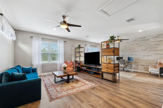 living room with wooden walls, hardwood / wood-style floors, ceiling fan, and a textured ceiling