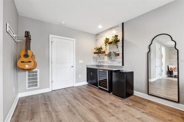 bar with light hardwood / wood-style floors, black fridge, and wine cooler