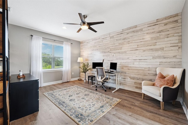 home office featuring wood-type flooring, ceiling fan, and wood walls