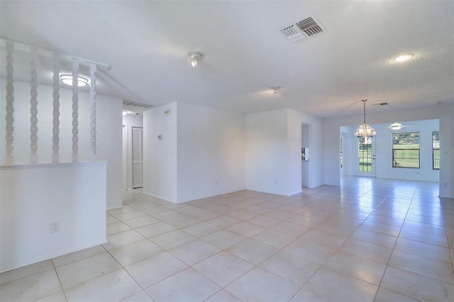 unfurnished room with a textured ceiling, light tile patterned flooring, and an inviting chandelier