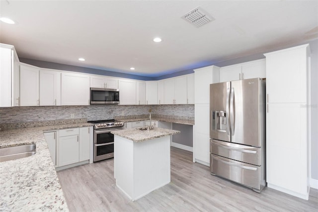 kitchen with decorative backsplash, light stone countertops, stainless steel appliances, white cabinets, and a kitchen island