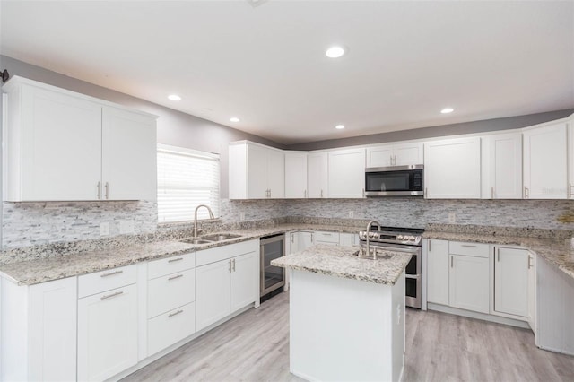 kitchen with a center island with sink, white cabinets, stainless steel appliances, and beverage cooler