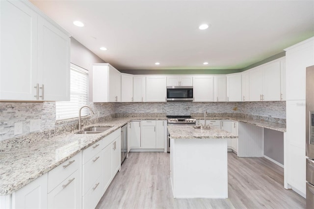 kitchen with a center island with sink, white cabinets, sink, light stone countertops, and appliances with stainless steel finishes