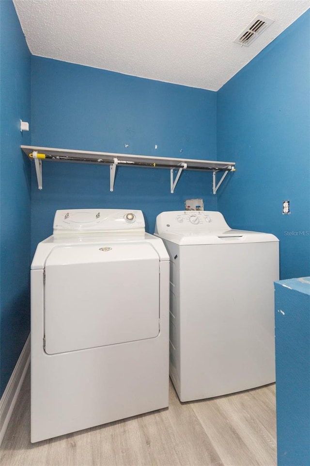 laundry area featuring light wood-type flooring, separate washer and dryer, and a textured ceiling