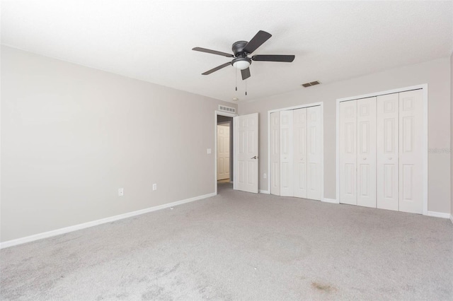 unfurnished bedroom with carpet flooring, ceiling fan, and two closets