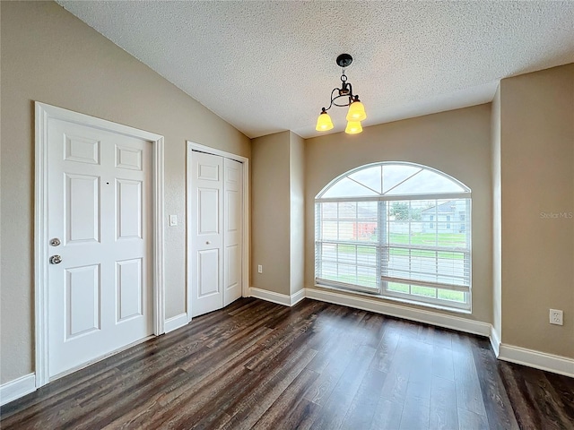 interior space with a textured ceiling, lofted ceiling, dark hardwood / wood-style floors, and a chandelier