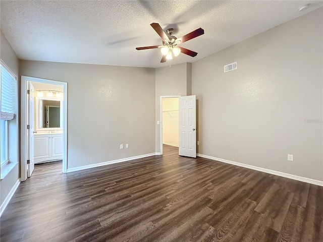 unfurnished bedroom with a spacious closet, a textured ceiling, dark hardwood / wood-style floors, ceiling fan, and ensuite bathroom