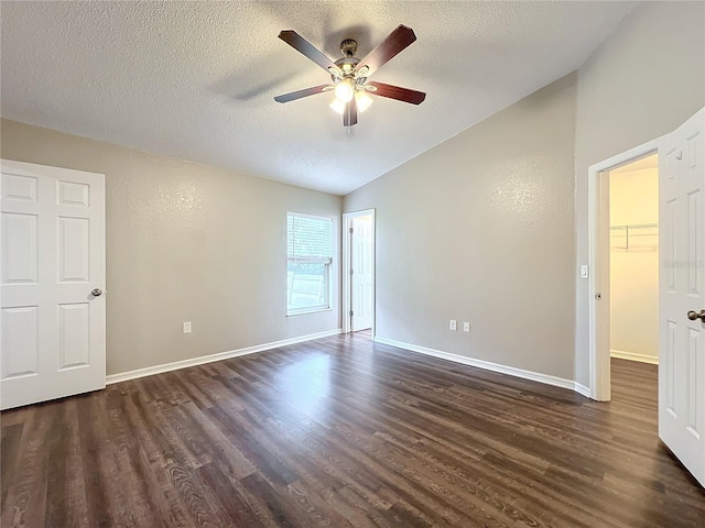 unfurnished bedroom with dark hardwood / wood-style flooring, vaulted ceiling, a textured ceiling, ceiling fan, and a spacious closet