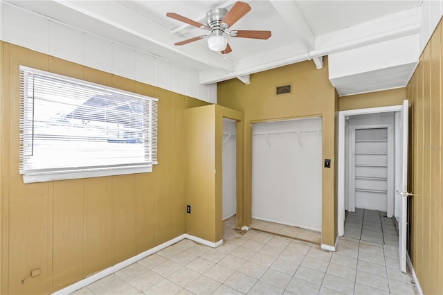 unfurnished bedroom featuring beamed ceiling, ceiling fan, wood walls, and light tile patterned flooring