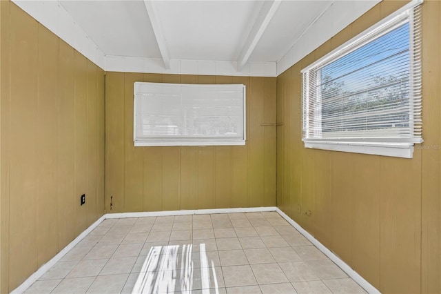 unfurnished room featuring beam ceiling, light tile patterned floors, and wood walls