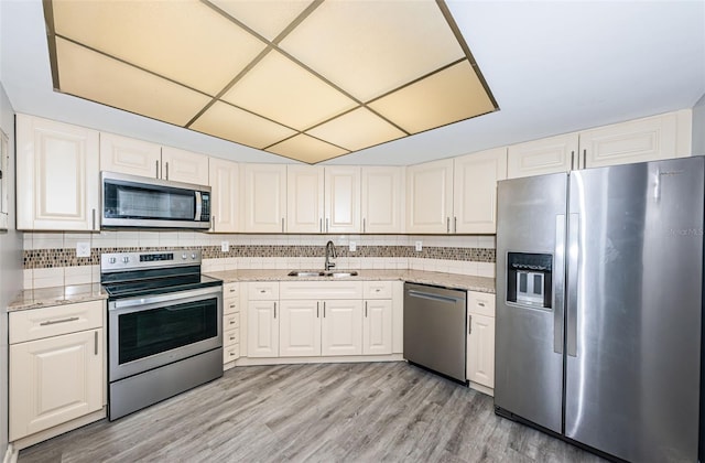 kitchen with tasteful backsplash, light stone counters, light wood-type flooring, appliances with stainless steel finishes, and sink