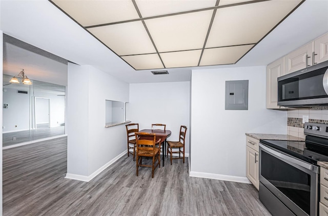 kitchen with electric panel, stainless steel appliances, decorative backsplash, and light wood-type flooring