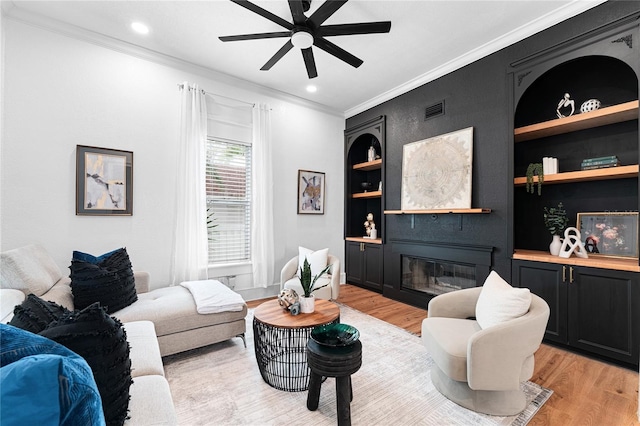 living room featuring ceiling fan, built in features, light wood-type flooring, and crown molding