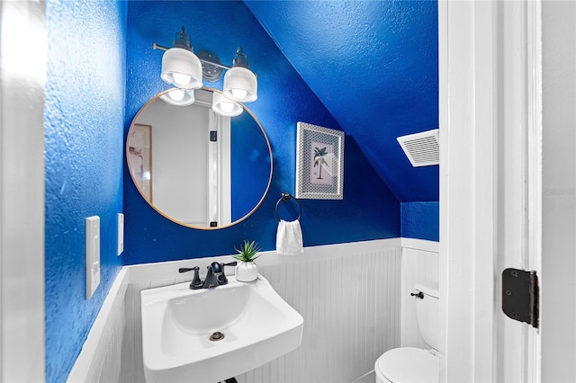 half bathroom featuring lofted ceiling, toilet, wainscoting, visible vents, and a sink