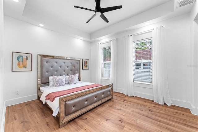 bedroom with light hardwood / wood-style flooring, ceiling fan, and a tray ceiling