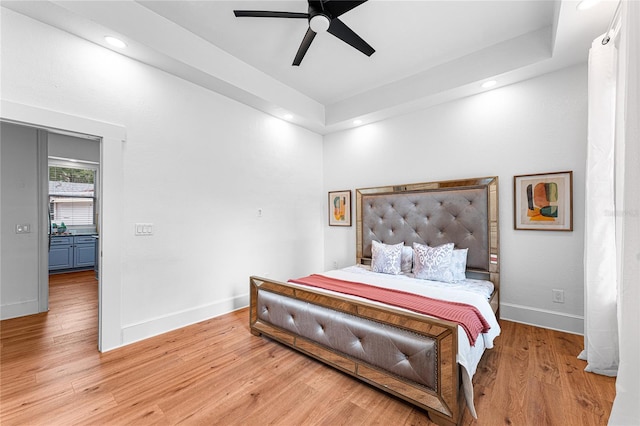 bedroom featuring light hardwood / wood-style floors, ceiling fan, and a tray ceiling