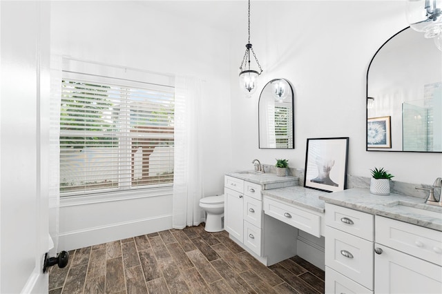 bathroom featuring wood-type flooring, toilet, vanity, and an inviting chandelier