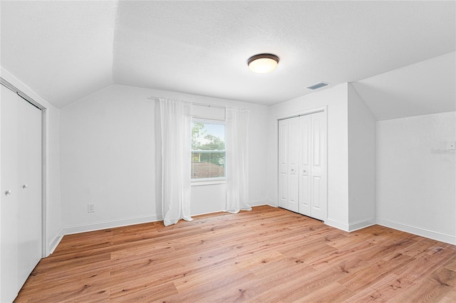 bonus room featuring lofted ceiling, a textured ceiling, visible vents, baseboards, and light wood-style floors