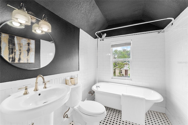 bathroom featuring sink, a textured ceiling, a bathing tub, lofted ceiling, and toilet