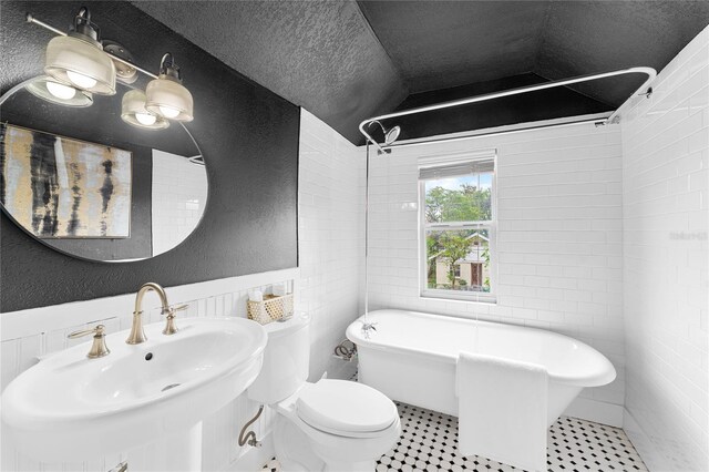 bathroom featuring lofted ceiling, toilet, a sink, a freestanding tub, and a textured wall